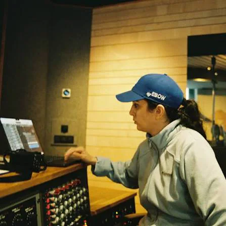 Ebow working at a recording-studio console while wearing a blue cap.